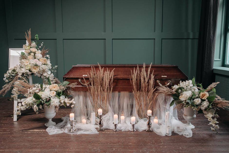 A floral arrangement featuring two large white vases filled with white roses, hydrangeas, and peonies, accented by dried pampas grass and greenery, positioned on either side of a vintage wooden casket